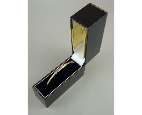 A contemporary 9ct hinged bangle retailed by Brooks and Bentley, the face decorated with seven captive rings of tri-coloured 