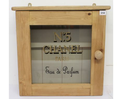 A stripped pine glazed wall or bathroom cabinet: the glazed door with gold and black painted &lsquo;No.5 Chanel Paris&rsquo; 