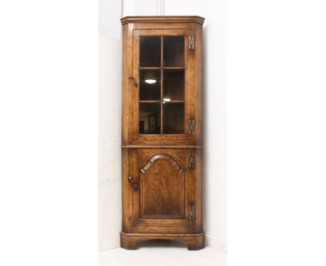 An early 18th century style oak part-glazed, floorstanding corner cupboard - late 20th century, the moulded top over a six-pa