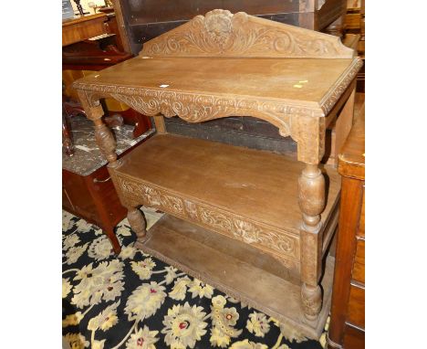 A circa 1900 heavily relief carved oak ledgeback three-tier buffet, having twin short green man mask carved handled drawers, 