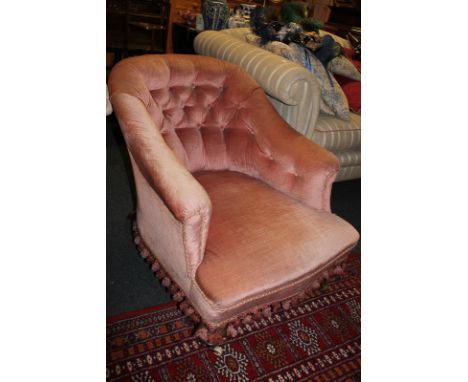 A button back low armchair upholstered in pink fabric, on turned legs and castors