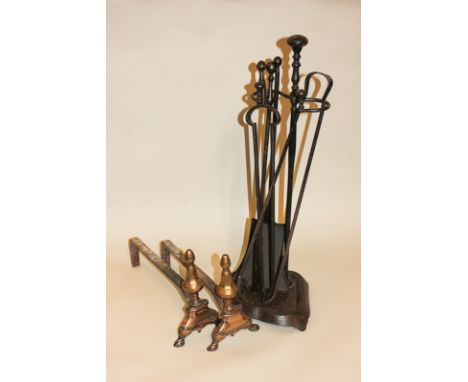 A pair of brass fire dogs, four fire tools including two tongs, shovel, poker in stand
