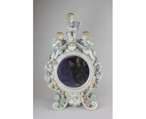 A continental porcelain mirror surround with circular bevelled mirror, with cherub surmount, and bocage floral decoration on 