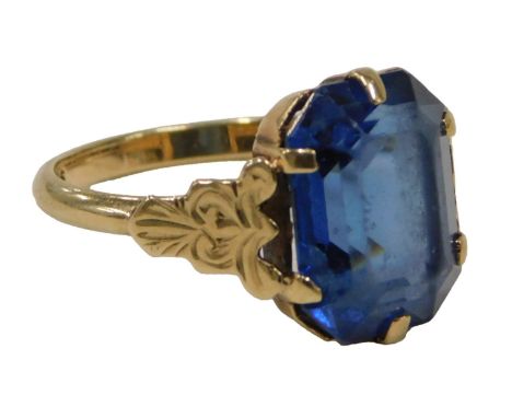 A blue stone set dress ring, the rectangular blue stone in claw setting, scroll design shoulders, yellow metal with rubbed ha