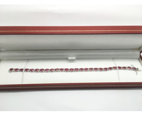 An 18ct white gold, oval ruby and round cut diamond line bracelet, rubies approx 12.23ct, diamonds approx 0.55ct, approx tota