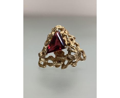 A vintage 9ct gold brooch set to the centre with a triangular-cut garnet, on an open textured conforming mount. 33mm by 36mm,