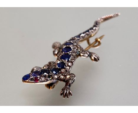A diamond-set novelty brooch modelled as a lizard, the body further set with a line of graduated sapphires, the eyes two ruby