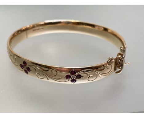 A diamond and ruby-set 9ct gold bangle, the hinged bangle set to one half with three flowerhead arrangements of stones, each 
