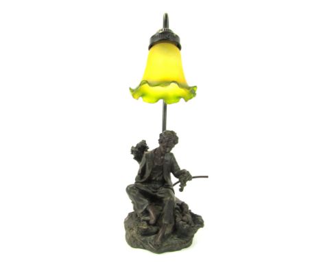 A 20thC table lamp, with frosted yellow and green trumpet glass shade above a figure of a young man seated beside two puppies