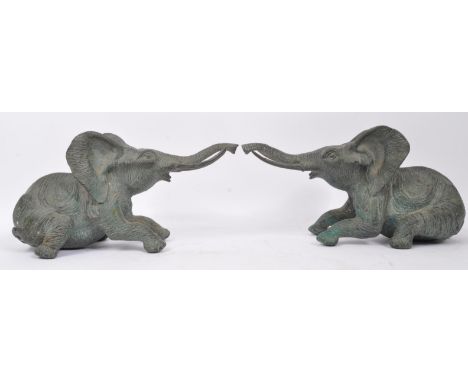 A pair of bronzed effect metal figurines sculptures of African elephants. In a seated rearing position with long trunk and tu