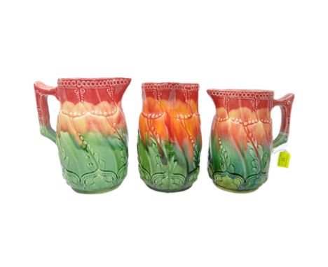 A collection of three matching vintage 20th Century ceramic pottery jugs. Having a red / green ground with textured foliate a