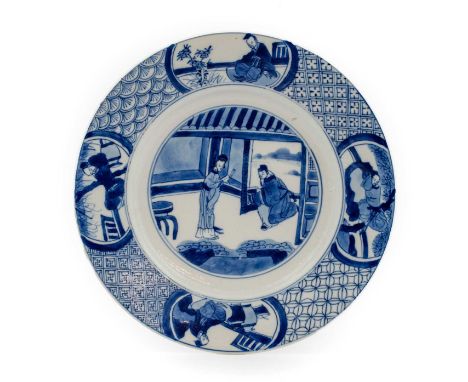 A Chinese Porcelain Plate, Kangxi mark and of the period, painted in underglaze blue with figures in an interior within a bro