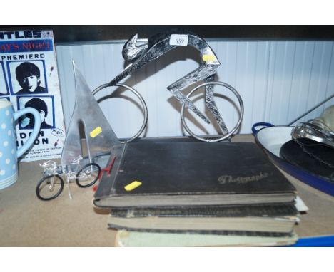 A stylised model boat; a stylised model of a figure on a bicycle; a wire work model of a bicycle and three albums containing 