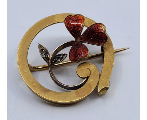 A precious yellow metal, enamel and diamond brooch,&nbsp; of circular form having scrolling clover to centre with red guilloc