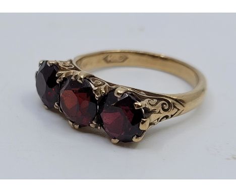 A 9ct. gold and garnet ring, set three mixed round cut garnets above scroll pierced gallery, size UK R. (gross weight 4.9g)