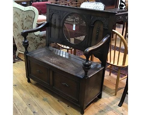 A 1920s oak hall bench, the plain top with centre canework circular panel flanked by arched panels, with scroll arms and lift