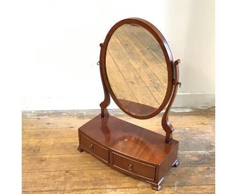 A reproduction mahogany bow fronted oval swing mirror raised on scroll end supports with bow fronted base fitted two drawers,