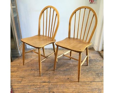 A pair of Ercol light ash spindle back kitchen chairs with shaped wood saddle seats, on turned tapered splay supports united 