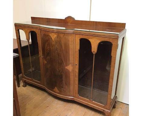 A 1930s bow fronted ledge back display cabinet, the top with moulded edge above a centre bow fronted inlaid panel door flanke