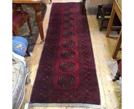 A Bokhara runner, the centre panel with nine octagons enclosed within a stylised leaf and flowerhead border, red field (261cm