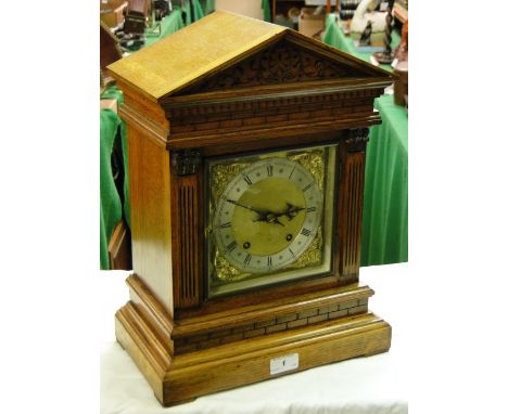 A carved oak cased mantel clock with brass dial and 2-train movement.
