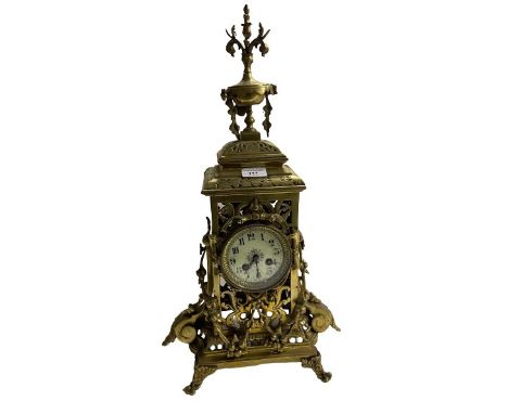 A 19th Century Baroque style pierced decorated brass Mantle Clock, the ornate finial over circular enamel dial on shaped base