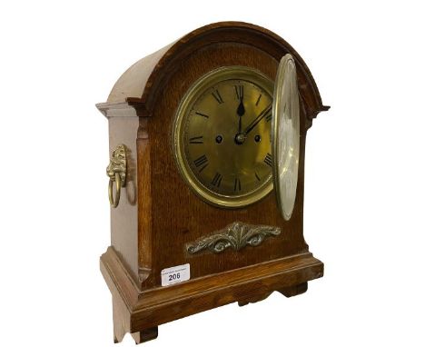 An Edwardian oak framed dome top Bracket Clock, with brass dial and Roman numerals, ormolu mount and brass mask drop handles.