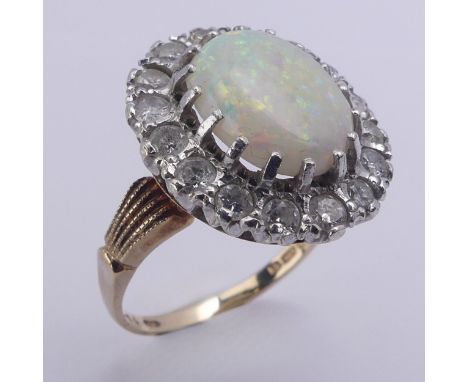 An opal and diamond cluster Ring, the central oval opal 12mm long surrounded by sixteen circular diamonds, approx. total weig