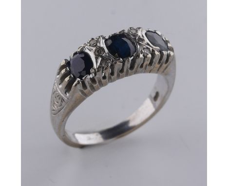 A three stone sapphire Ring, the cushion shaped facetted stones with three diamond points vertically set between, all mounted