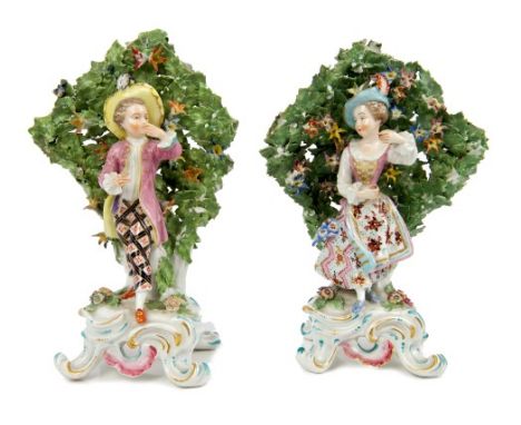 Pair of 18th century Bow porcelain dancing figures, each standing in front of a flowering tree bocage, an rococo scroll bases