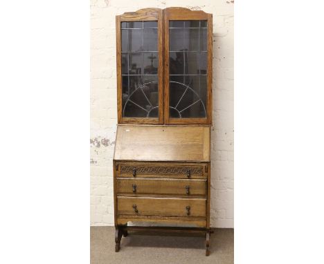 An oak bureau bookcase with leaded glass doors, carved and raised on bracket feet with a cross stretcher.