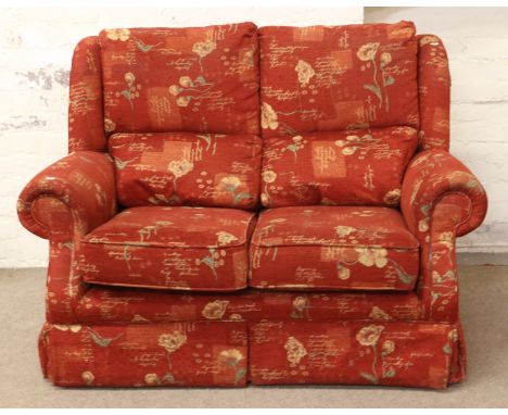 A red upholstered two seater sofa with floral decoration.