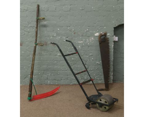 A collection of garden tools to include scythe, tree saw and hand plough.