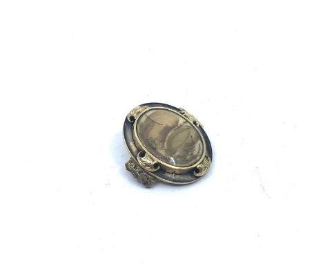 A 19th century mourning brooch, a oval glass containing strands of light coloured hair, surrounded by unmarked gold brackets,