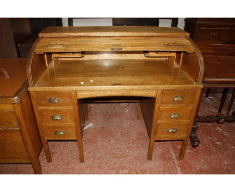 An early 20th Century oak roll top desk, with tambour front and six short drawers on square section legs, bearing brass plaqu