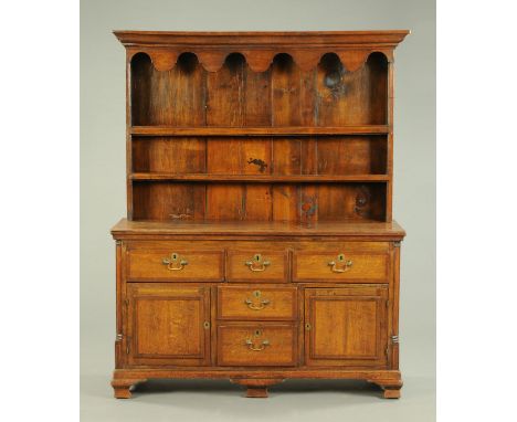 A Georgian oak dresser with Delft rack, the base fitted with a series of drawers and cupboards being crossbanded and all rais