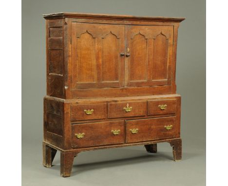 A Georgian oak cupboard, with moulded cornice above a pair of panelled doors, the base fitted with a series of drawers with b