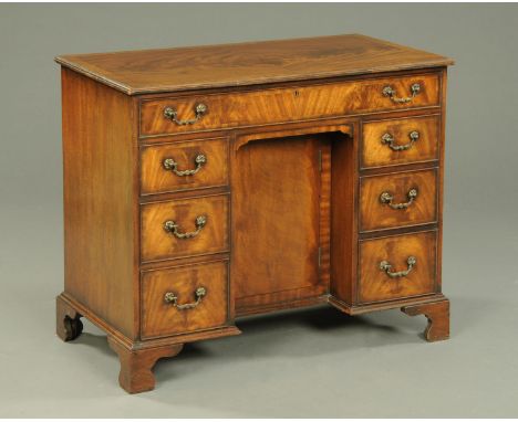 A George III style mahogany kneehole desk, crossbanded and fitted with a series of drawers and recessed cupboard, all raised 