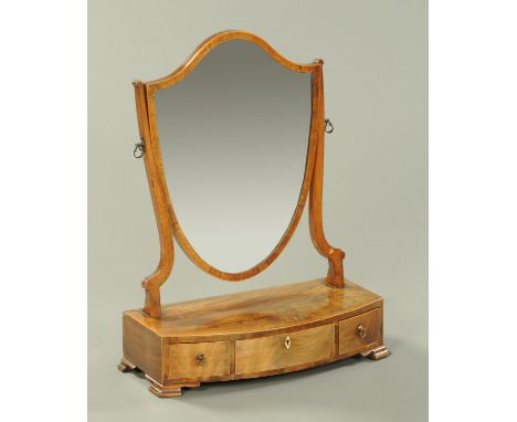 A George III mahogany toilet mirror, shield shaped, with bowfronted base fitted with frieze drawers and raised on bracket fee