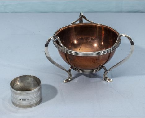 A copper bowl with a silver holder and a silver napkin ring