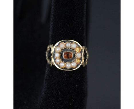 An 18ct gold mourning ring with central orange stone, black enamel border and seed pearl frame (some missing) ornately decora