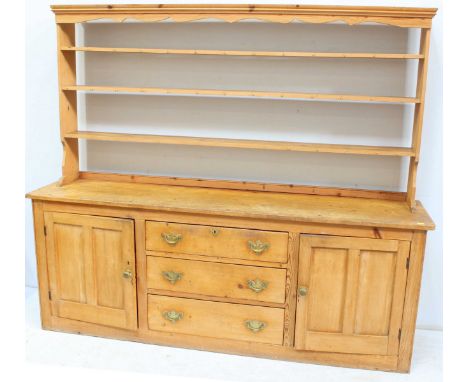 A large pine kitchen dresser with shaped cornice above three long open back shelves and hooks, the base with three long gradu