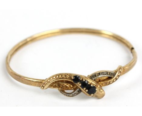 A 9ct yellow gold bangle decorated with snake motif set with three graduated round cut sapphires and diamond chips to shanks,