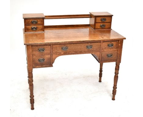 An Edwardian oak writing table, surmounted by two banks of drawers above and arrangement of five further frieze drawers, each
