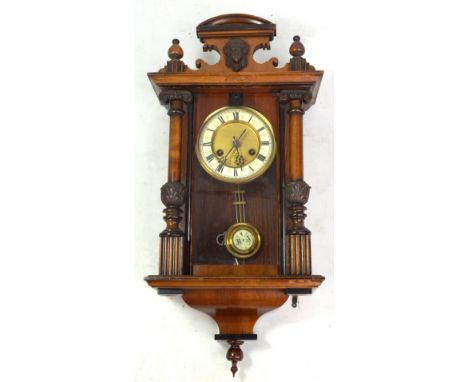 An early 20th century wall clock, the porcelain chapter ring set with Roman numerals, the glazed door flanked by twin carved 