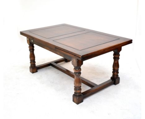 A reproduction oak drawleaf table raised on ring turned baluster supports united by a stretcher, length when extended approx 