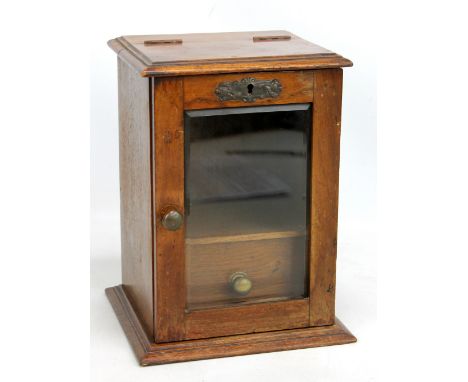 An Edwardian oak smoker's cabinet with hinged top above single glazed door enclosing pipe rack and drawer, height 28.5cm.