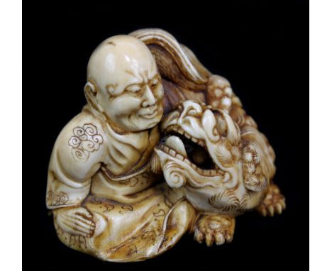 HUNGETSU; a good 19th century Japanese carved ivory netsuke of Rakkan seated with a shishi, signed to base, height 3.7cm, wid