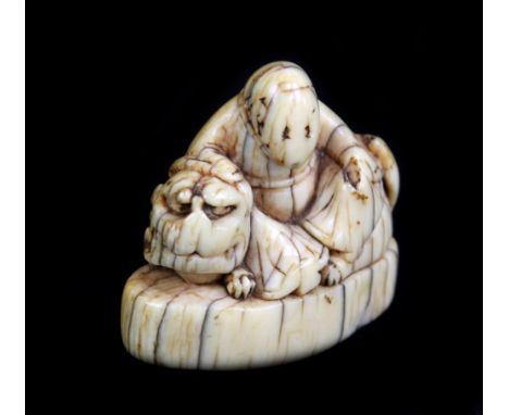 A 17th century Japanese carved ivory netsuke of Rakkan with shishi on a base, height 4cm.Additional InformationThe netsuke is