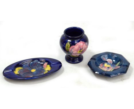 MOORCROFT; a navy ground 'Magnolia' pattern tubeline decorated vase, height 9cm, and two floral decorated ashtrays (3).Additi
